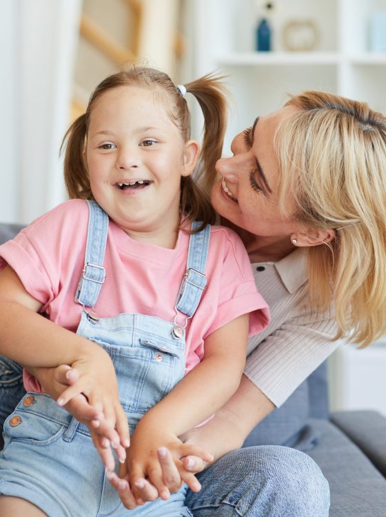 Young mother embracing her disabled child while they sitting on sofa in the room